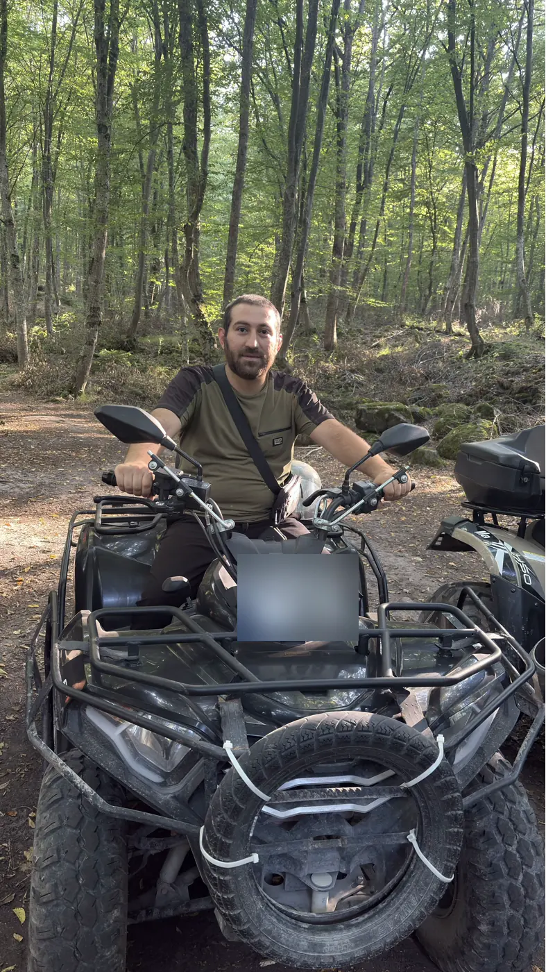 An ATV parked on a dirt track in the forest with its rider